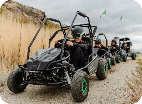 Kids in helmets riding a line of electric buggies along a gravel trail